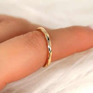 May include: A thin gold band ring with a twisted, textured design.