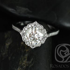 May include: A silver engagement ring featuring a large, round, clear centre stone surrounded by smaller diamonds. The ring has a delicate, ornate design.