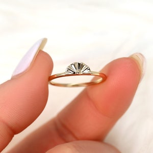 May include: A gold ring featuring a sun-shaped design. The ring is thin and delicate, with a smooth finish.