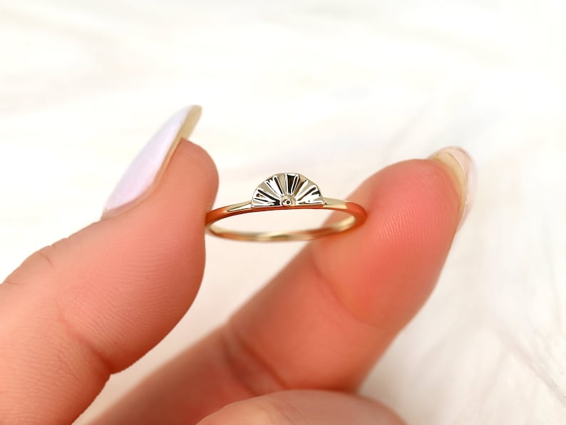 May include: A gold ring featuring a sun-shaped design. The ring is thin and delicate, with a smooth finish.