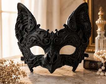 May include: A matte black masquerade mask featuring intricate, raised scrollwork and filigree patterns. The mask is shaped with pointed, bat-like ears and a central nose bridge, covering the eye area with two large, almond-shaped openings.