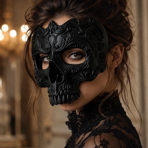 May include: A matte black skull mask featuring intricate embossed scrollwork and floral patterns across the forehead and cheekbones. The mask covers the upper face, revealing the eyes, and includes a detailed nose and teeth structure.