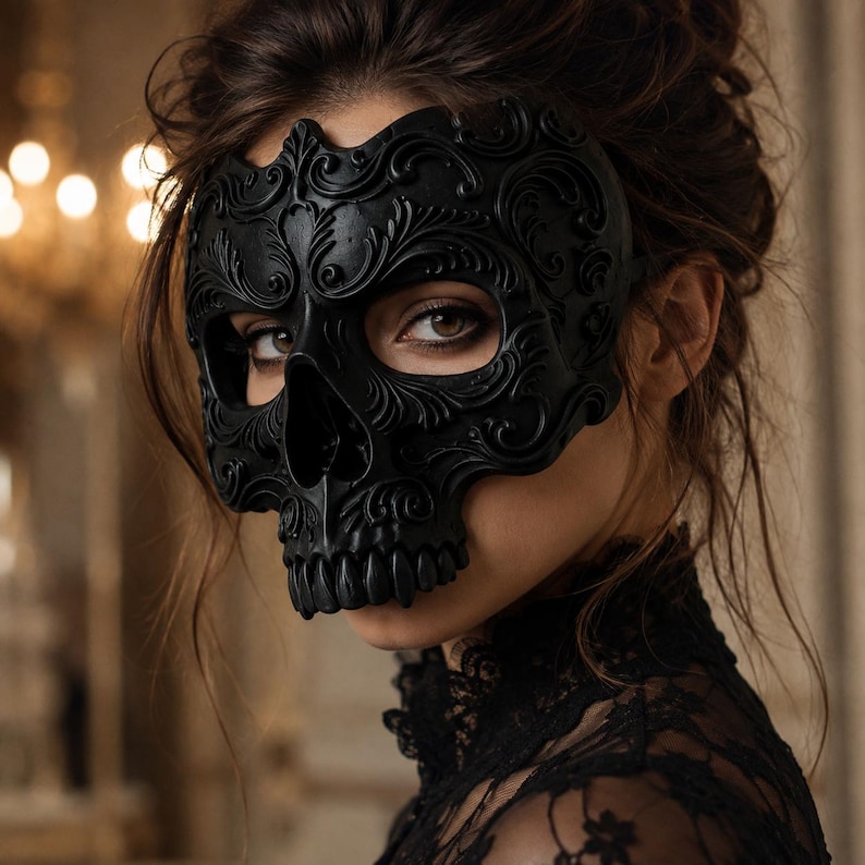 May include: A matte black skull mask featuring intricate embossed scrollwork and floral patterns across the forehead and cheekbones. The mask covers the upper face, revealing the eyes, and includes a detailed nose and teeth structure.