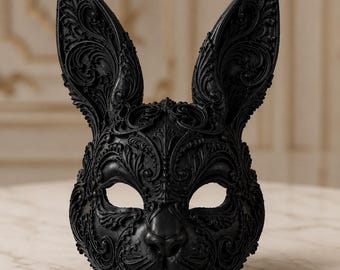 May include: A matte black rabbit mask featuring intricate, raised scrollwork and filigree patterns across the entire surface. The mask includes two tall, pointed ears, almond-shaped eye openings, and a sculpted nose and mouth area.