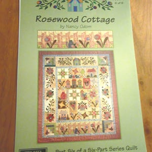 Op de afbeelding: Een lichtgroen instructieboekje getiteld Rosewood Cottage door Nancy Odom, deel zes van een zesdelige quiltserie. De omslag bevat een afbeelding van een quilt met een hekwerkrand, bloemmotieven en kleine illustraties van huizen.