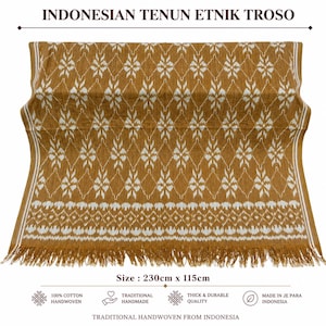 Puede incluir: Un textil amarillo mostaza con un patrón de diamantes y flores en blanco y bordes con flecos. La tela mide 230cm x 115cm. El texto superior dice INDONESIAN TENUN ETNIK TROSO, y el inferior incluye 100% COTTON HANDWOVEN, TRADITIONAL HANDMADE, THICK & DURABLE QUALITY, MADE IN JE PARA INDONESIA, y TRADITIONAL HANDWOVEN FROM INDONESIA.