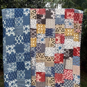 May include: A rectangular patchwork quilt featuring a variety of square fabric blocks in shades of blue, red, mustard yellow, and white. The quilt displays diverse patterns including floral, geometric, chevron, and block-printed designs.