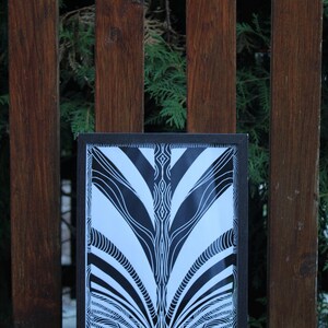 May include: A rectangular framed print featuring a high-contrast black and white graphic design. The artwork displays symmetrical, flowing lines and intricate, repeating patterns that radiate from the center, encased in a simple dark frame.