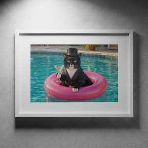 May include: A framed wall art print featuring a black and white tuxedo cat wearing a black top hat and a black tuxedo jacket. The cat is floating in a bright pink inflatable pool ring in blue water while holding a martini glass with an olive.
