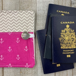 May include: A pink and grey fabric passport holder with a white anchor pattern and a white button closure. The holder is next to two Canadian passports.