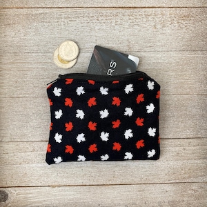 May include: A small black zippered pouch with a red and white maple leaf pattern. The pouch is open and a black card with the word "RS" is visible inside.