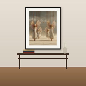 May include: A framed wall art print featuring a surreal scene of multiple figures with large, translucent wings suspended by thin vertical strings. The figures wear pleated white dresses and stand on a flat, light-colored surface under a cloudy sky.