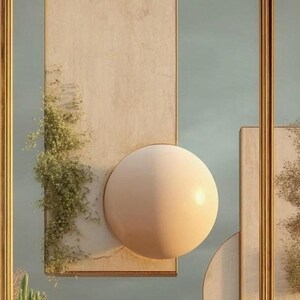 May include: A wall art piece featuring a large, smooth, beige sphere mounted on a rectangular, light-colored panel. A trailing green plant grows along the left side of the panel. The composition is framed by thin, vertical gold-colored metal bars.