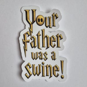 May include: A die-cut sticker featuring the text Your father was a SWINE! in a gold-colored, gothic-style font with black shading. The letter O in the word Your is replaced by a circular icon with two small black dots, all on a white background.
