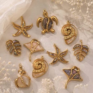 May include: A collection of ten gold-toned metal charms featuring various shapes including sea turtles, starfish, stingrays, spiral shells, and tropical leaves. Each charm is inlaid with iridescent abalone shell or smooth white mother-of-pearl.