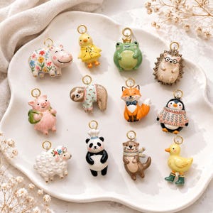May include: A collection of twelve small animal charms with gold-tone loops, including a floral hippo, yellow chick in a raincoat, frog with a crown, hedgehog with glasses, pig, sloth, fox with a bow tie, penguin, sheep, panda chef, otter, and duck.
