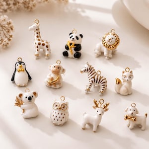 Puede incluir: Una colección de once pequeños dijes de animales que incluyen una jirafa, panda, león, pingüino, mono, cebra, zorro, koala, búho, ciervo y perro. Cada dije está elaborado con esmalte blanco y detalles en metal dorado con una pequeña argolla.