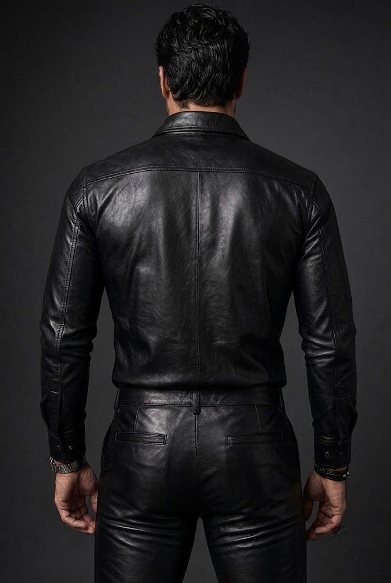 Op de afbeelding: Een zwart leren overhemd met lange mouwen, een puntkraag en zichtbare stiksels, gecombineerd met een bijpassende zwarte leren broek met achterzakken en een tailleband met riemlussen, gezien vanaf de achterkant.