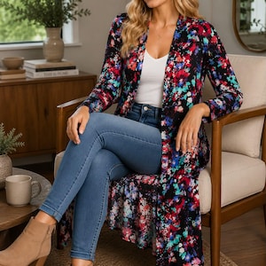 May include: A long-sleeved, open-front duster cardigan featuring a vibrant floral pattern in shades of red, blue, pink, and white against a black background, worn over a white V-neck top, blue denim jeans, and tan suede ankle boots.