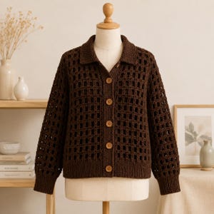 May include: A dark brown long-sleeve cardigan featuring an open-knit grid pattern, a classic collar, and five light-colored buttons down the front. The garment is displayed on a mannequin, showcasing the textured crochet-style knit construction.