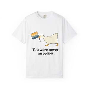 May include: A white short-sleeve t-shirt featuring a graphic of a white goose with an orange beak and feet holding a small flag with horizontal stripes of yellow, white, blue, and dark grey. The text "You were never an option" is printed below.
