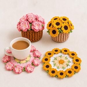 Peut inclure: Deux pots de fleurs au crochet avec des fleurs roses et jaunes, accompagnés de deux dessous de verre circulaires assortis. Un dessous de verre soutient une tasse en céramique blanche remplie de café brun. Textures en laine et motifs floraux.