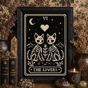 Può includere: Un'opera a punto croce incorniciata con un design di carta dei tarocchi in nero e crema intitolata The Lovers. L'immagine raffigura due gatti scheletrici uno di fronte all'altro con un cuore, una luna crescente, stelle e montagne in stile pixel.