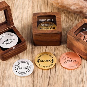 May include: Three square wooden boxes with glass lids and three circular metal decision coins. The coins feature engraved names including Brian, Thomas, William, Mark, Sarah, and Steve, along with text such as Who Will Decide and Flip To Decide.