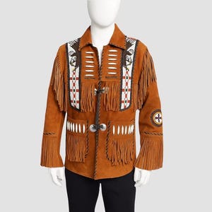 May include: A tan suede jacket featuring long fringe detailing on the chest and sleeves. The front is adorned with white bone-like accents, beaded panels depicting eagle motifs, and silver-toned metal closures. A circular patch is on the sleeve.