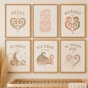Può includere: Un set di sei stampe da parete incorniciate con parole e illustrazioni māori in tonalità terra tenui. Le stampe includono testi come AROHA, WHĀNAU, PŌ MĀRIE, KIA KAHA e HE TAONGA KOE, esposte in cornici di legno chiaro sopra una culla.