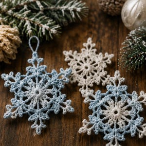 May include: Three crocheted snowflake ornaments featuring intricate lace patterns. One snowflake is solid white, while the other two are crafted with a blend of light blue and white yarn. Each piece includes a small loop at the top for hanging.