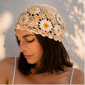 Peut inclure: Un bonnet en crochet orné d'un motif répétitif de marguerites. Les fleurs présentent des pétales blancs et des cœurs jaune vif, reliés par une structure en fil beige clair ajouré. Le bonnet possède un bord festonné et une forme arrondie.