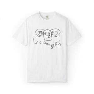 May include: A white short-sleeved t-shirt featuring a black hand-drawn style illustration of a ram head centred on the chest. Below the ram illustration, the text Los Angeles is written in a matching black, casual, handwritten script style.
