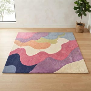 May include: A rectangular area rug featuring a multi-colored abstract pattern of wavy, organic shapes. The design incorporates shades of navy blue, light blue, pink, magenta, purple, orange, cream, and olive green in a soft, tufted texture.