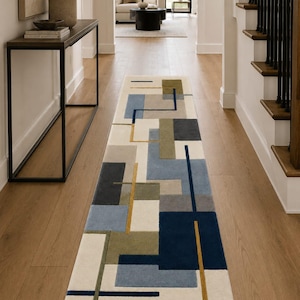 May include: A long rectangular runner rug featuring a geometric pattern of overlapping blocks and lines in shades of navy blue, light blue, olive green, gray, and cream. The design consists of solid color rectangles and thin linear accents.