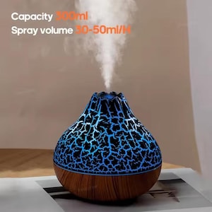 May include: A teardrop-shaped essential oil diffuser with a wood grain base and a black upper section featuring a glowing blue crackle pattern. A white mist rises from the top. Text reads: Capacity 300ml, Spray volume 30-50ml/H.