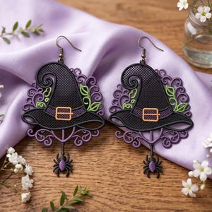 May include: A pair of black witch hat earrings featuring a purple filigree border, a small orange buckle, and a dangling purple spider charm. The earrings are constructed with a mesh-like texture and include a metal hook for attachment to the ear.