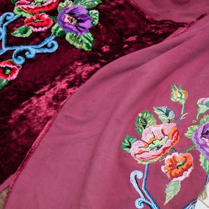 Puede incluir: Una tela de terciopelo color burdeos intenso y una tela malva m&aacute;s clara, ambas con bordados florales vibrantes. El bordado incluye flores rojas, rosas y moradas con hojas verdes y tallos azul claro en espiral, creando un patr&oacute;n detallado.