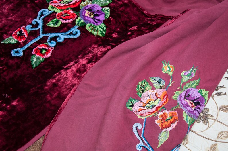 Puede incluir: Una tela de terciopelo color burdeos intenso y una tela malva m&aacute;s clara, ambas con bordados florales vibrantes. El bordado incluye flores rojas, rosas y moradas con hojas verdes y tallos azul claro en espiral, creando un patr&oacute;n detallado.