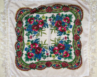 May include: A white square scarf with a floral pattern. The pattern features red, blue, and green flowers on a white background. The scarf has a white fringe border.