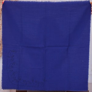 Pode incluir: Um quadrado de tecido azul sólido com um design bordado decorativo no canto inferior esquerdo.