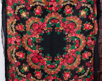May include: A black shawl with a floral pattern in shades of red, green, gold, and white. The shawl has a fringe border.