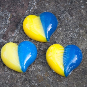 May include: Three heart-shaped objects, each divided in half with a yellow top and a blue bottom. The objects are arranged in a triangular pattern on a gray, textured surface.