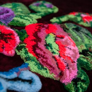 Puede incluir: Una tela de terciopelo color burdeos oscuro con un patr&oacute;n de bordado floral en relieve y texturizado. El dise&ntilde;o incluye flores grandes y vibrantes en tonos rosa ne&oacute;n, rojo brillante, verde lima y azul claro, hechas con hilo grueso.
