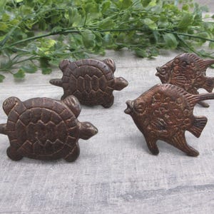 May include: Four metal cabinet knobs with a dark bronze finish, featuring two turtle-shaped designs and two fish-shaped designs. Each knob has a textured surface with detailed carvings representing the shells of the turtles and the scales of the fish.