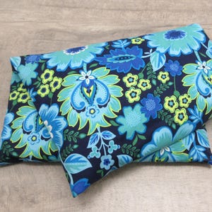 May include: Two folded fabric items with a vibrant floral pattern. The design features large blue and turquoise flowers with green accents on a navy blue background. The fabric appears soft and likely used for home decor or crafts.