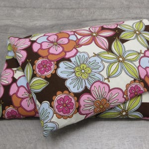 May include: Two decorative pillows with a floral pattern. The pillows feature large flowers in shades of pink, orange, blue, and green on a brown background. The flowers are set against a white backdrop.