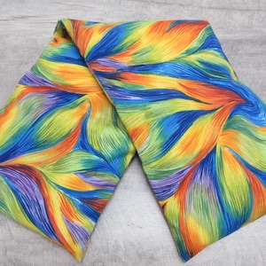 May include: A rectangular fabric heating pad featuring a vibrant, multi-colored abstract pattern of swirling, flame-like shapes in shades of bright blue, orange, yellow, green, and purple, with a soft, textured surface throughout the entire piece.