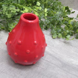 May include: A red ceramic vase with a textured, dotted surface. The vase is shaped like a pear and has a wide opening at the top.