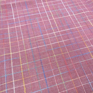 May include: A close-up of a red fabric with a multi-coloured plaid pattern. The fabric has white, blue, yellow, and red stripes.